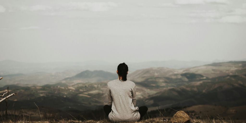 woman sitting on cliff overlooking mountains during daytime