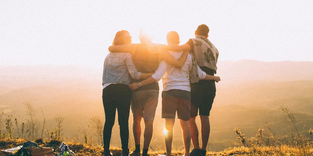 four person hands wrap around shoulders while looking at sunset