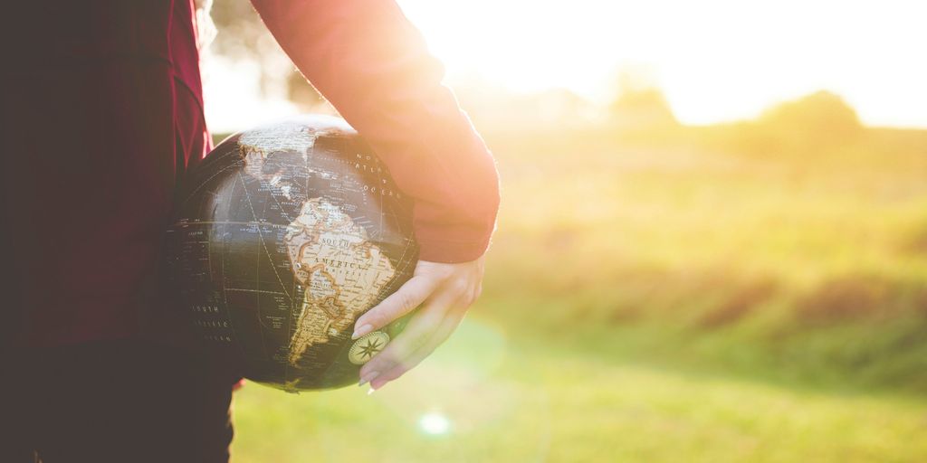 person holding black and brown globe ball while standing on grass land golden hour photography