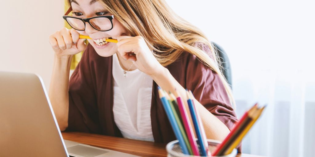 woman biting pencil while sitting on chair in front of computer during daytime